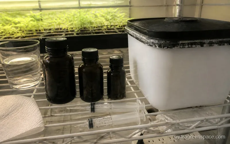 Three General Hydroponics Flora Trio bottles lined up next to a reservoir with measuring syringes