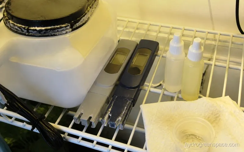 Digital pH meter and EC/PPM meter next to a hydroponic reservoir with pH up and down solution bottles
